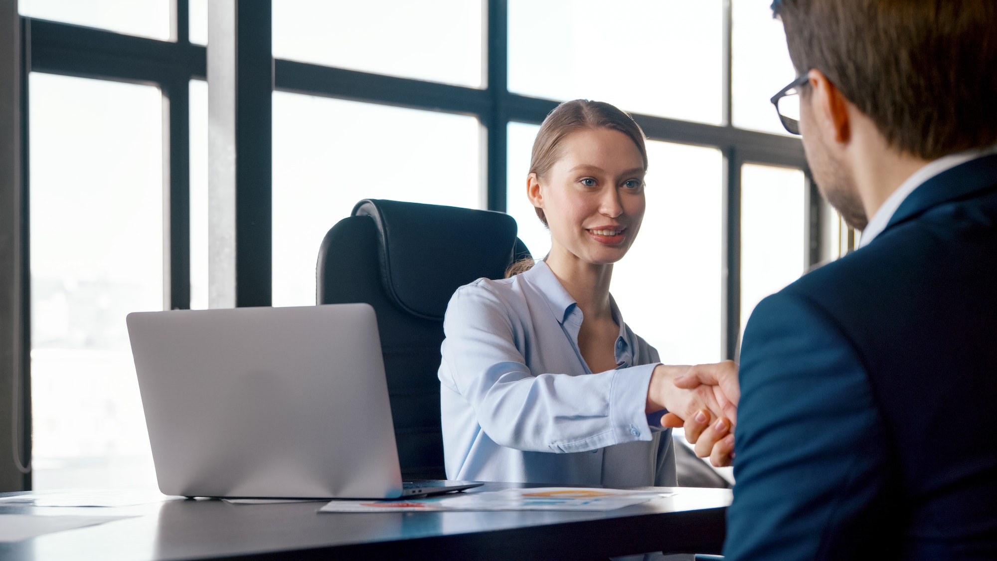 Young businesswoman hiring new colleague shaking hands after successful job interview